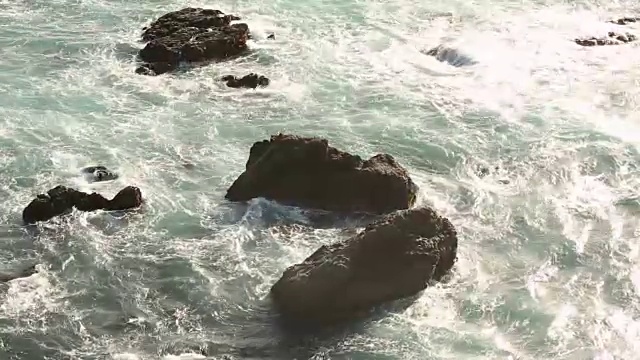 大苏尔的岩石海岸线，海浪拍打着海岸，阳光照耀着。视频素材