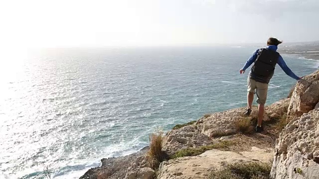 一名年轻人在刮风的日子沿着多岩石的山脊攀登视频素材