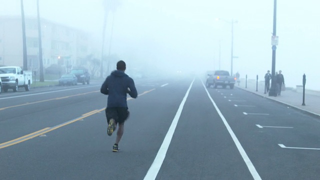 一个年轻人在海滩边一个住宅区的街道上跑步。视频素材