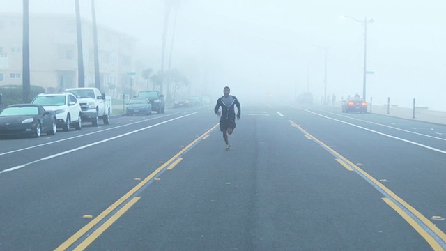 一个年轻人在海滩边一个住宅区的街道上跑步。视频素材