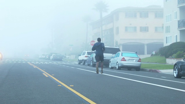 一个年轻人在海滩边一个住宅区的街道上跑步。视频素材