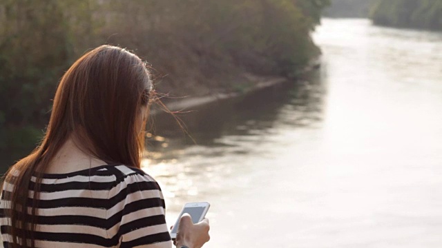 年轻的亚洲女人用智能手机看湖景视频素材