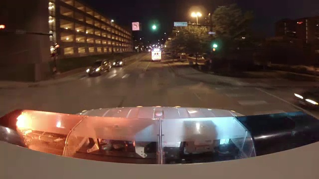 从一辆救护车的顶部看第二辆救护车，在晚上沿着街道跑到城市医院，画面底部有闪烁的灯光。视频素材