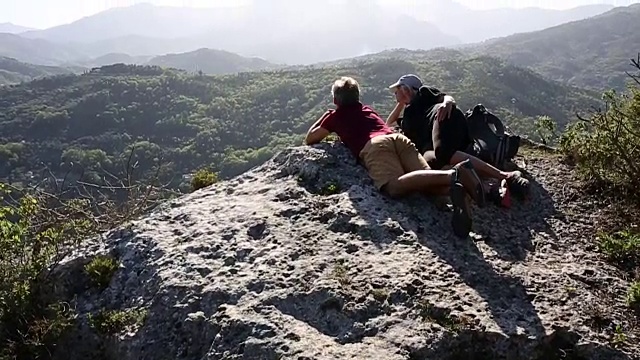 徒步旅行的夫妇在岩壁上放松，眺望山谷视频素材