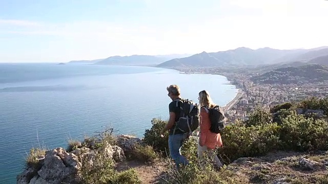 一对徒步情侣走到山顶，眺望大海和群山视频素材