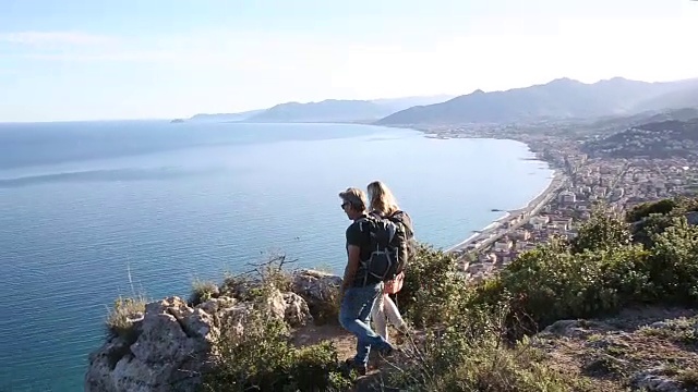 一对徒步情侣走到山顶，眺望大海和群山视频素材