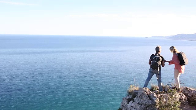 一对徒步情侣走到山顶，眺望大海和群山视频素材