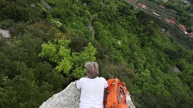 一名男性徒步旅行者在岩壁上放松，眺望下面的山谷视频素材