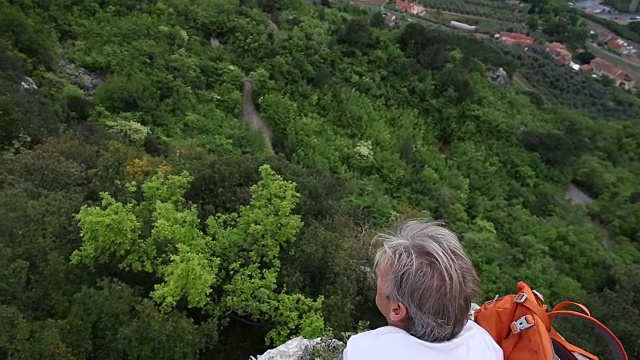 一名男性徒步旅行者在岩壁上放松，眺望下面的山谷视频素材