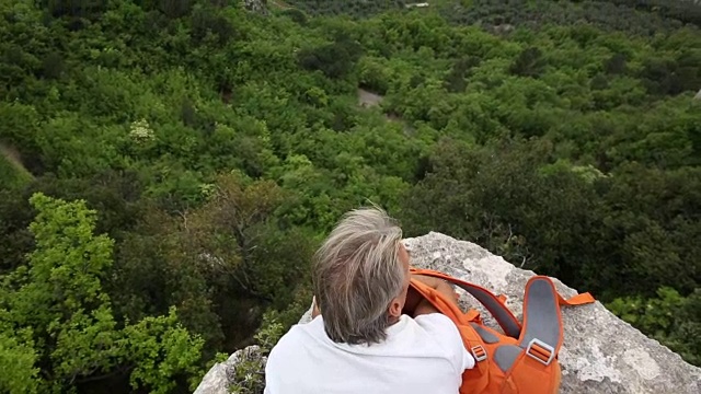 一名男性徒步旅行者在岩壁上放松，眺望下面的山谷视频素材