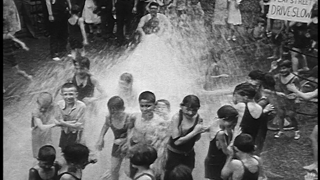 1930年高角度人群中的孩子站在从消防栓喷水的纽约街道视频素材