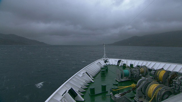 一艘船正沿着挪威暴风骤雨的北部海岸线行驶，从船头拍摄的POV跟踪镜头。视频素材