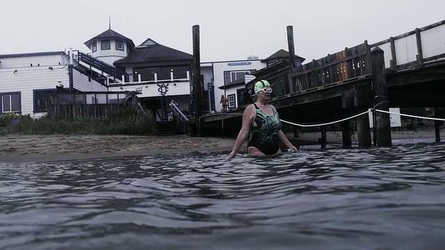 高级女游泳运动员进入水和开始游泳在旧金山湾寒冷的灰色水域。视频下载