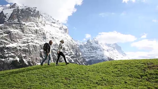 一对徒步情侣爬上了雪山下的绿色草地视频素材