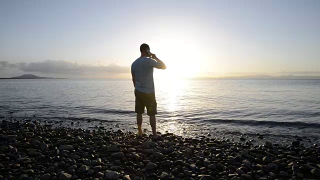 一个男人在海滩上看着日落接电话视频素材