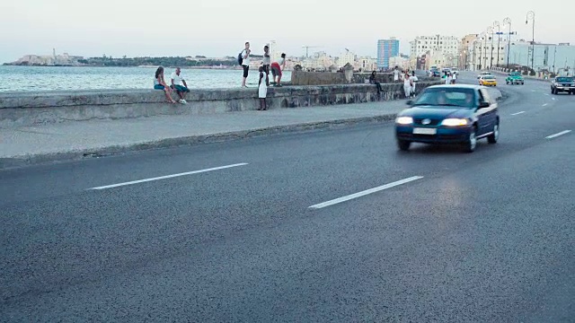 哈瓦那古巴马列孔路建立拍摄。街道上有经典的美国老爷车，人们在墙上行走或停留。视频素材