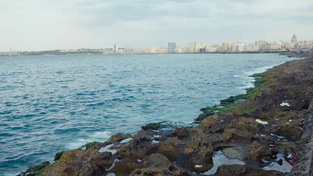 哈瓦那古巴马列康防波堤与天际线的前景。日落时分，蓝色的海浪拍打在加勒比海的岩石上。视频素材