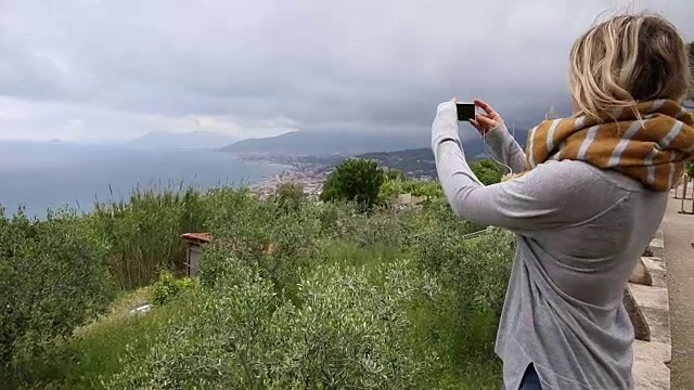 年轻女子用智能手机拍下了山和远处的海视频素材