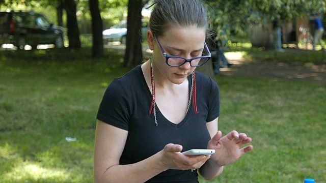 一个年轻女子在公园里用她的智能手机视频素材