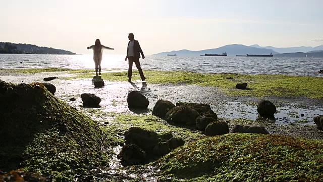 一对夫妇沿着潮岩走向大海，躲避着海水视频素材