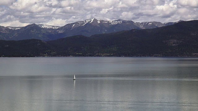 孤独的帆船在平静的山湖与白雪覆盖的春天山的背景。视频素材