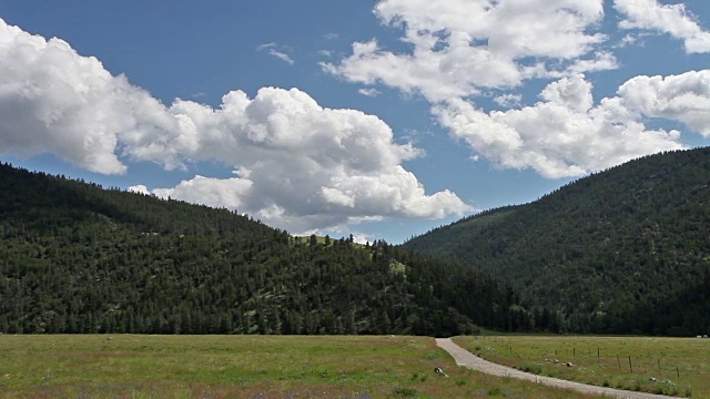 阴影在绿色的田野上滚动，背景是土路和山脉。视频素材