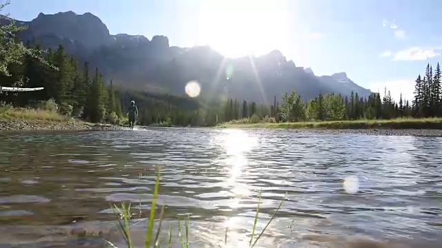 越野赛跑运动员在山脚下的河流浅滩上奔跑视频素材