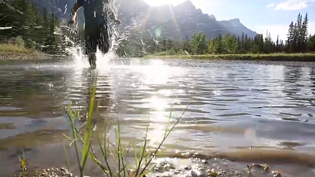 越野赛跑运动员在山脚下的河流浅滩上奔跑视频素材