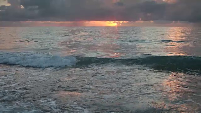 太阳从地平线升起时，海岸上有柔和的波浪视频素材