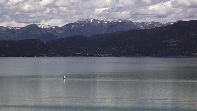 孤独的帆船在平静的山湖与白雪覆盖的春天山的背景。视频素材