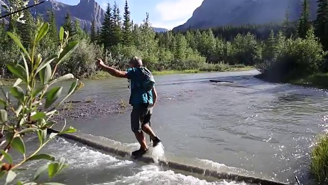 一名男性徒步旅行者用淹没在水中的原木涉水过山溪视频素材