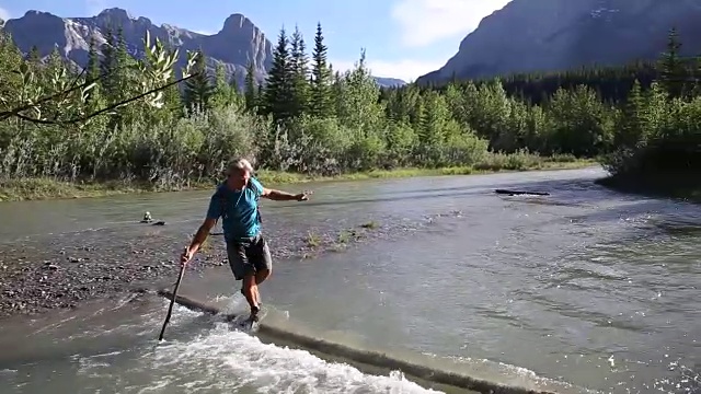 一名男性徒步旅行者用淹没在水中的原木涉水过山溪视频素材