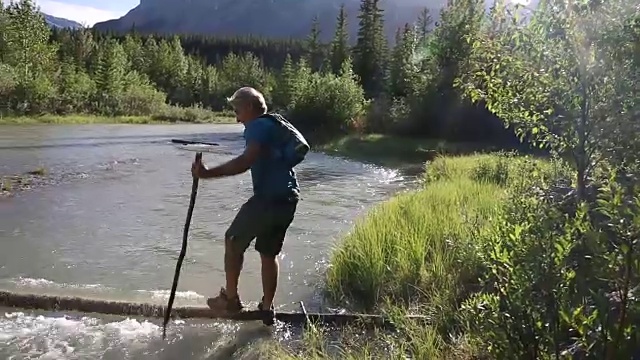 一名男性徒步旅行者用淹没在水中的原木涉水过山溪视频素材