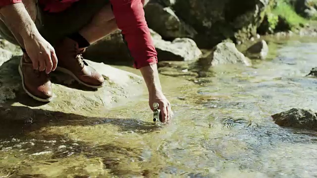 一个登山家从山涧中往瓶子里灌水。视频素材