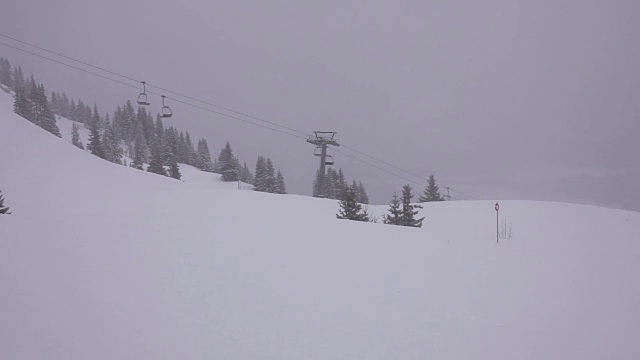 山上有雾，还在下雪。空的升降椅在底部运行。视频素材