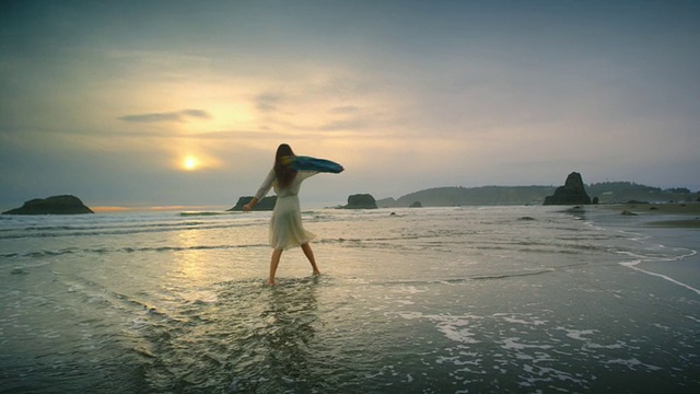 年轻女子在日落时分的海洋海滩上散步和旋转视频素材