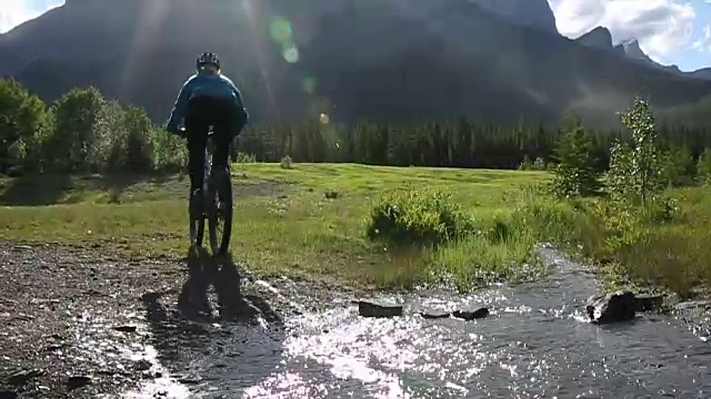 女山地自行车骑手穿过溪流，继续进入草地视频素材