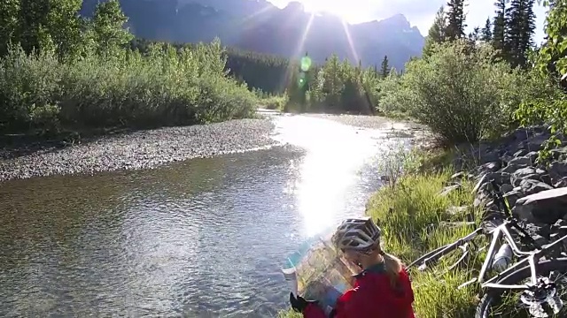 一位骑山地车的女性在小溪边休息，看地图视频素材