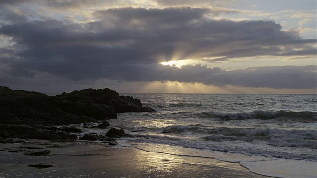 当云朵在夕阳前掠过时，海浪撞击岩石视频素材