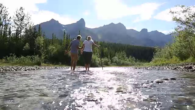 一对夫妇涉水穿过山间小溪，从卵石滩到对岸视频素材