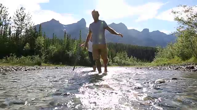 一对夫妇涉水穿过山间小溪，从卵石滩到对岸视频素材