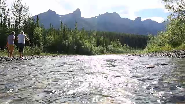 一对夫妇涉水穿过山间小溪，从卵石滩到对岸视频素材