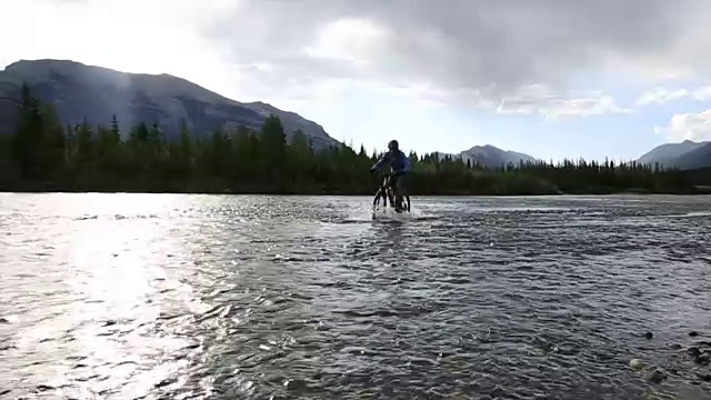 男性山地自行车骑手穿过河流远离遥远的山脉视频素材