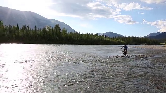 男性山地自行车骑手穿过河流远离遥远的山脉视频素材