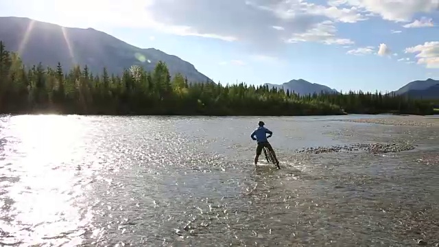 男性山地自行车骑手横渡河流向远处的山脉视频素材