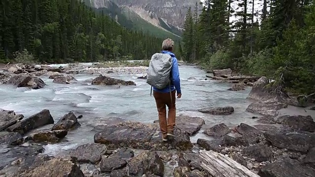 一名男性徒步者走到河边，眺望着暴风雨般的山脉视频素材