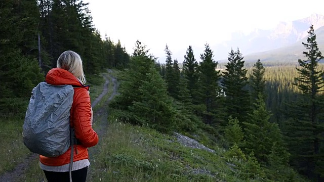 清晨，一名女性徒步旅行者沿着山路行走视频素材