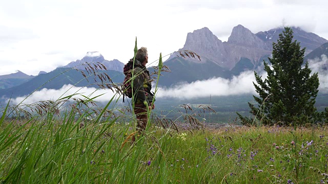 一名男性徒步旅行者在雨后走进草地，眺望群山视频素材