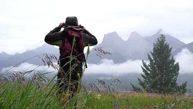 一名男性徒步旅行者在雨后走进草地，眺望群山视频素材