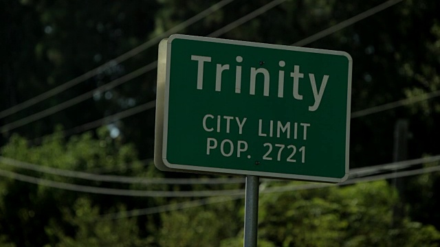 高速公路镇的标志，上面写着，“Trinity City Limit pop”。一辆车从公路上开过。视频素材